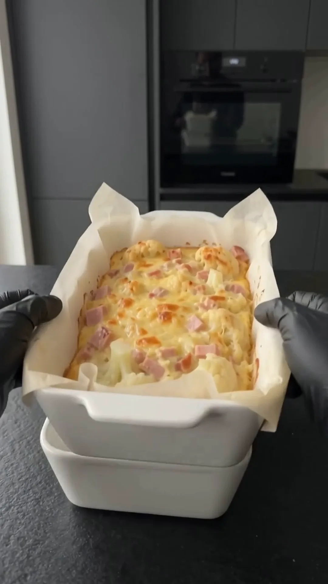 Cheesy Cauliflower and Smoked Turkey Casserole Bake – A person is holding a baking dish with a smoked turkey and cheese mixture