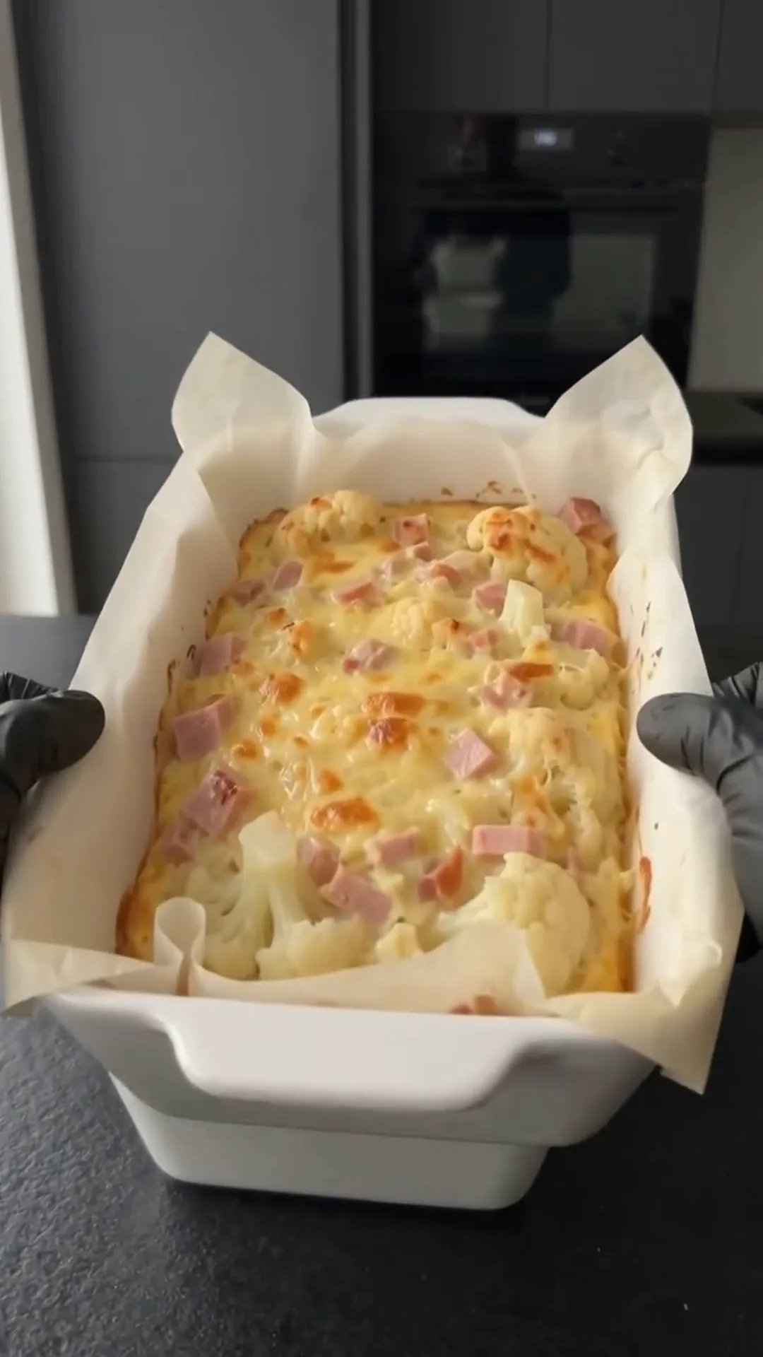 Cheesy Cauliflower and Smoked Turkey Casserole Bake – A person is holding a baking tray with a cauliflower and smoked turkey casserole