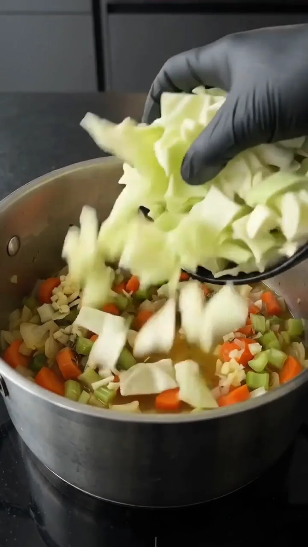 Comforting Homemade Cabbage Soup with Fresh Vegetables – Adding chopped vegetables to a pot of soup