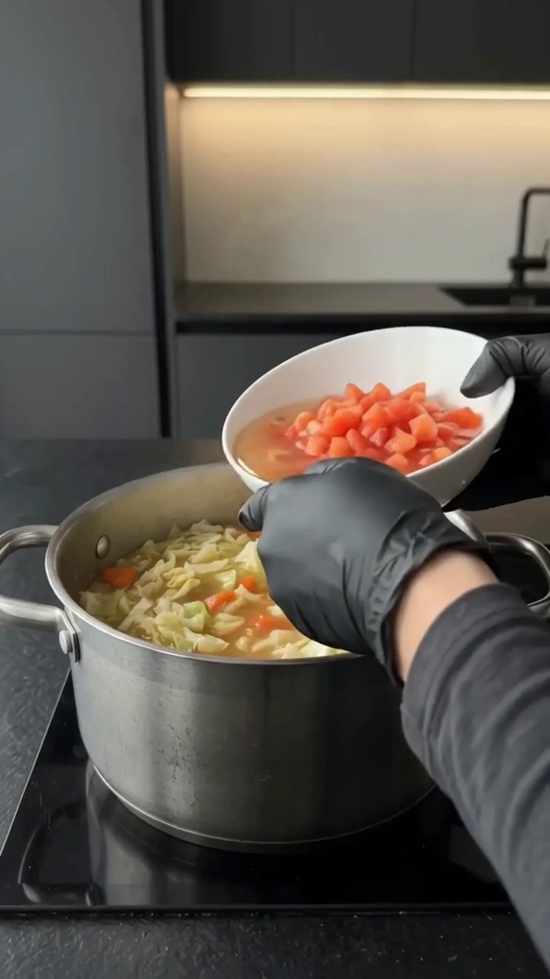 Comforting Homemade Cabbage Soup with Fresh Vegetables – person adding chopped tomatoes to a pot of soup