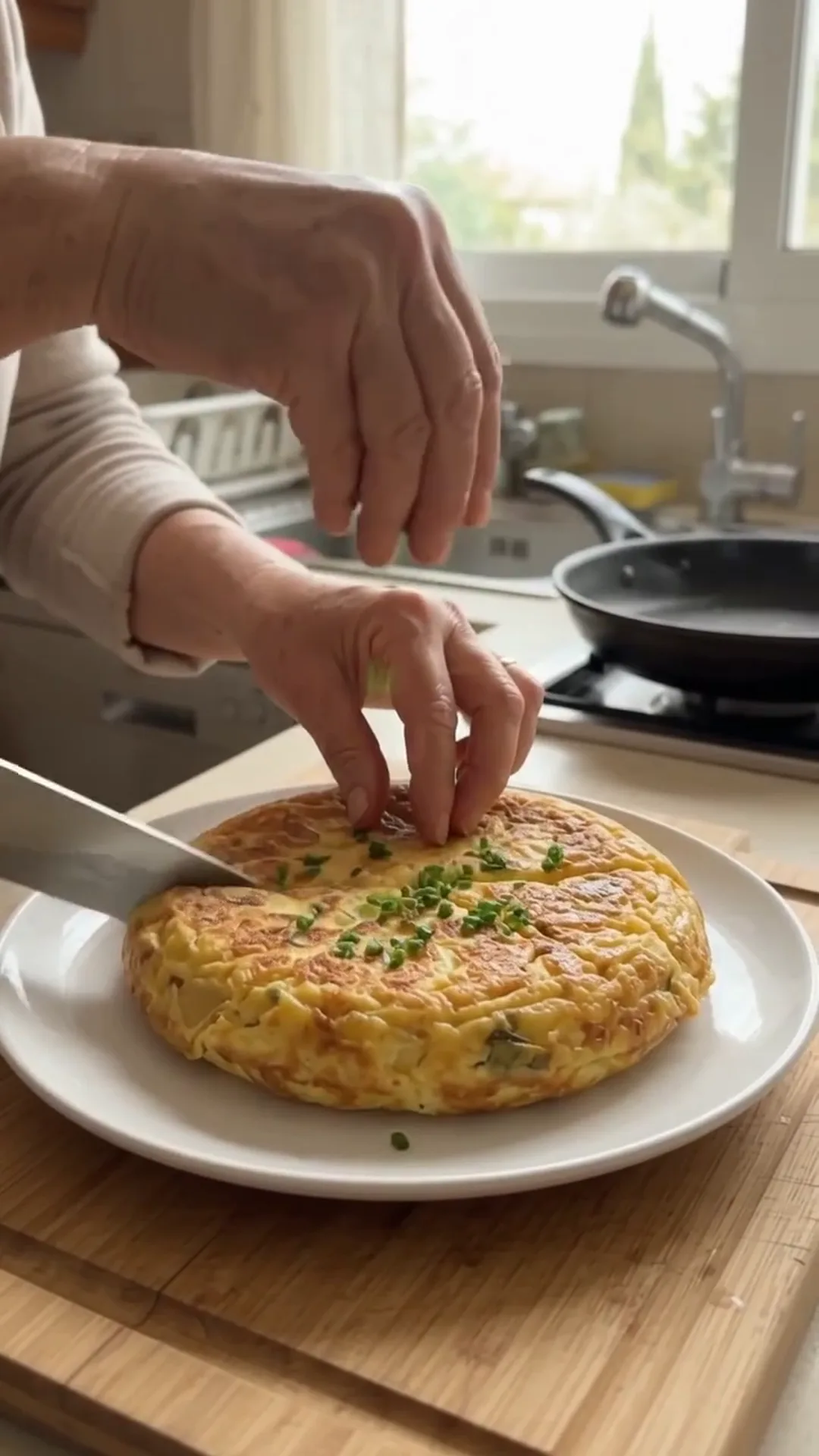 Crispy Potato Crust and Egg Breakfast Skillet Pizza – A person is garnishing a round omelette with chives