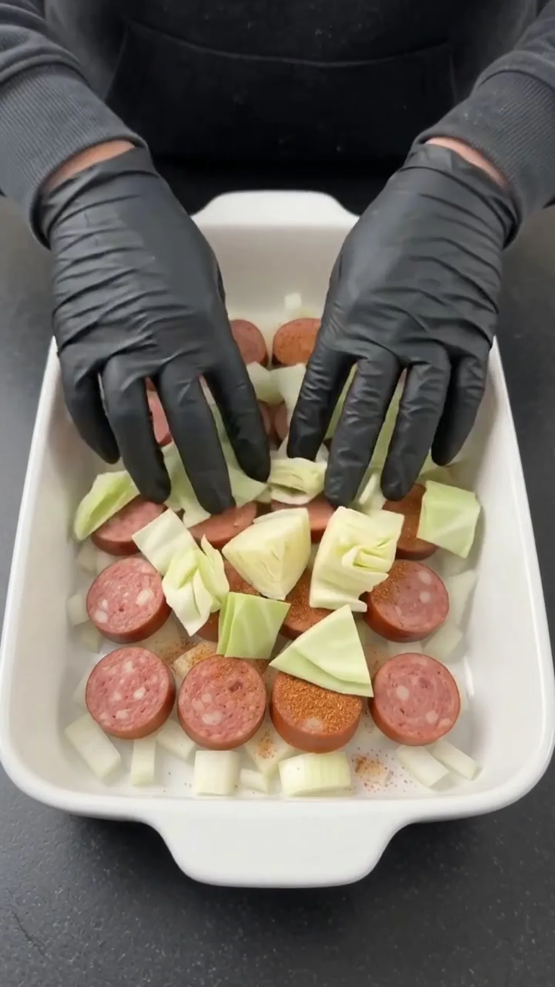 Easy Baked Cabbage and Smoked Beef Sausage Recipe – person placing ingredients in a baking dish