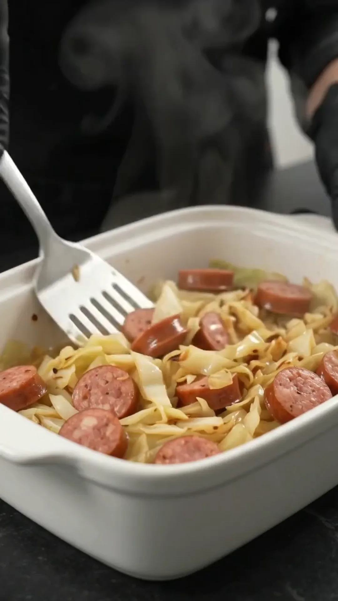Easy Baked Cabbage and Smoked Beef Sausage Recipe – person stirring a dish of sausage and cabbage in a pan