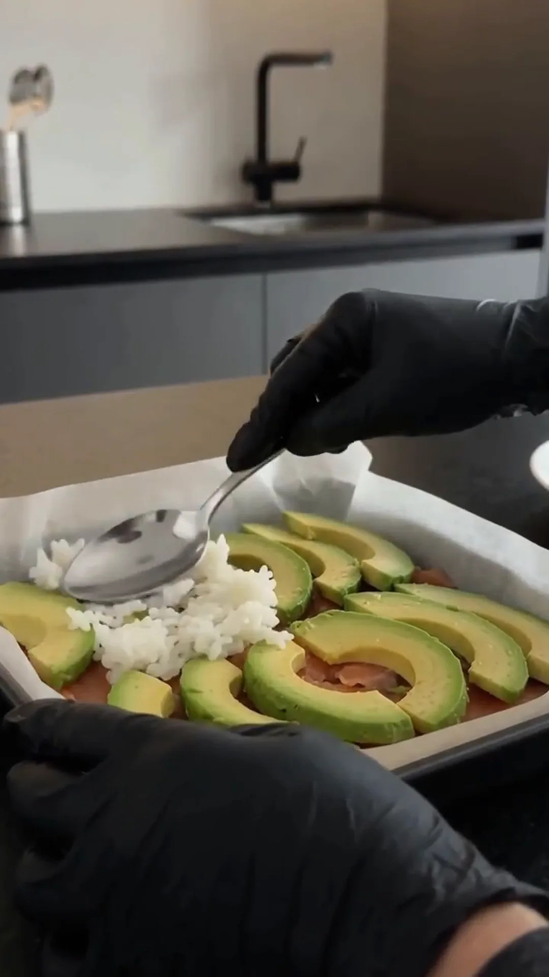 Easy Salmon Avocado Sushi Squares with Spicy Mayo – person adding rice to sliced avocado in a baking tray