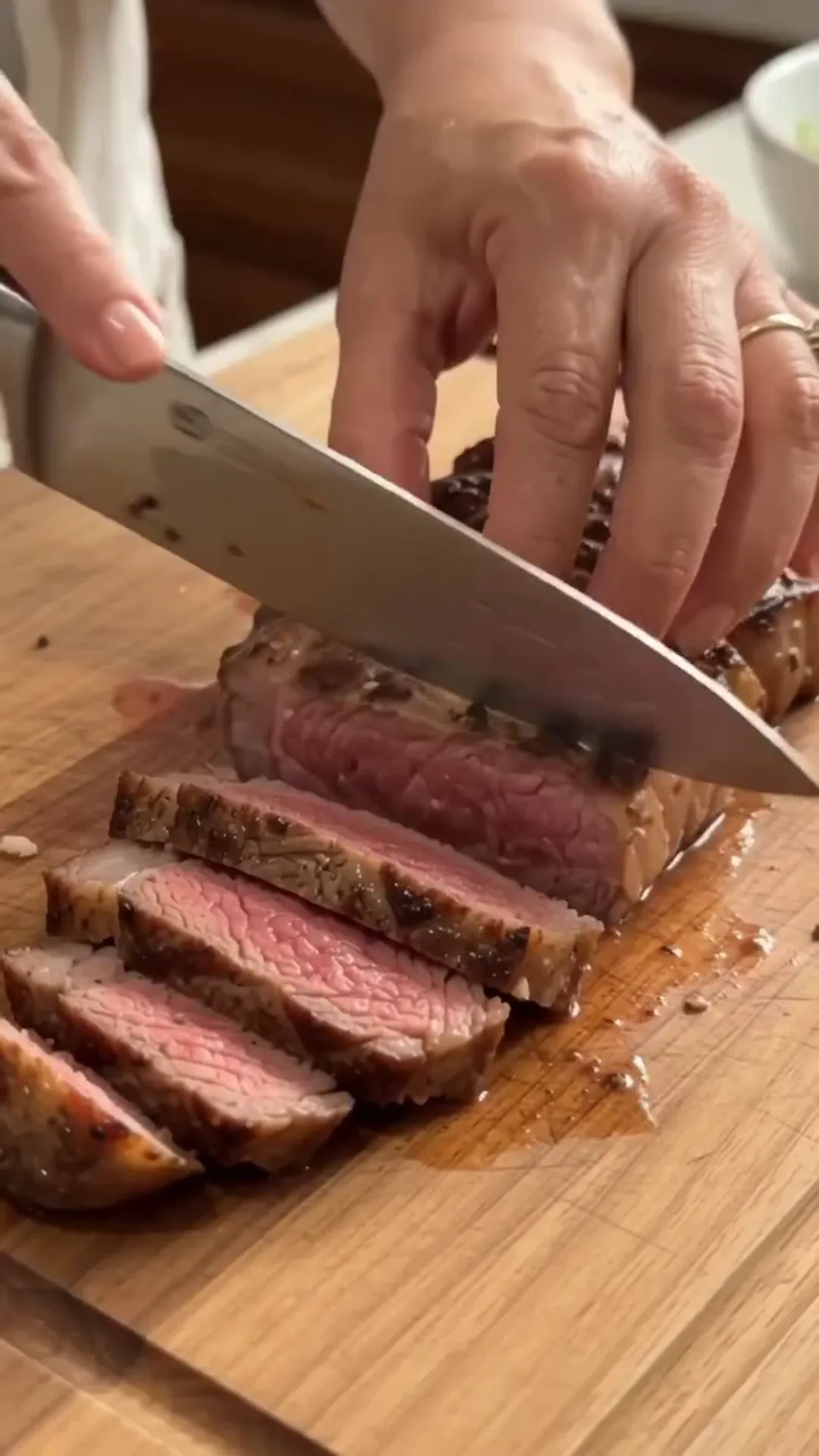 Garlic Butter Loaded Steak Baked Potatoes – A person is slicing cooked meat on a wooden cutting board