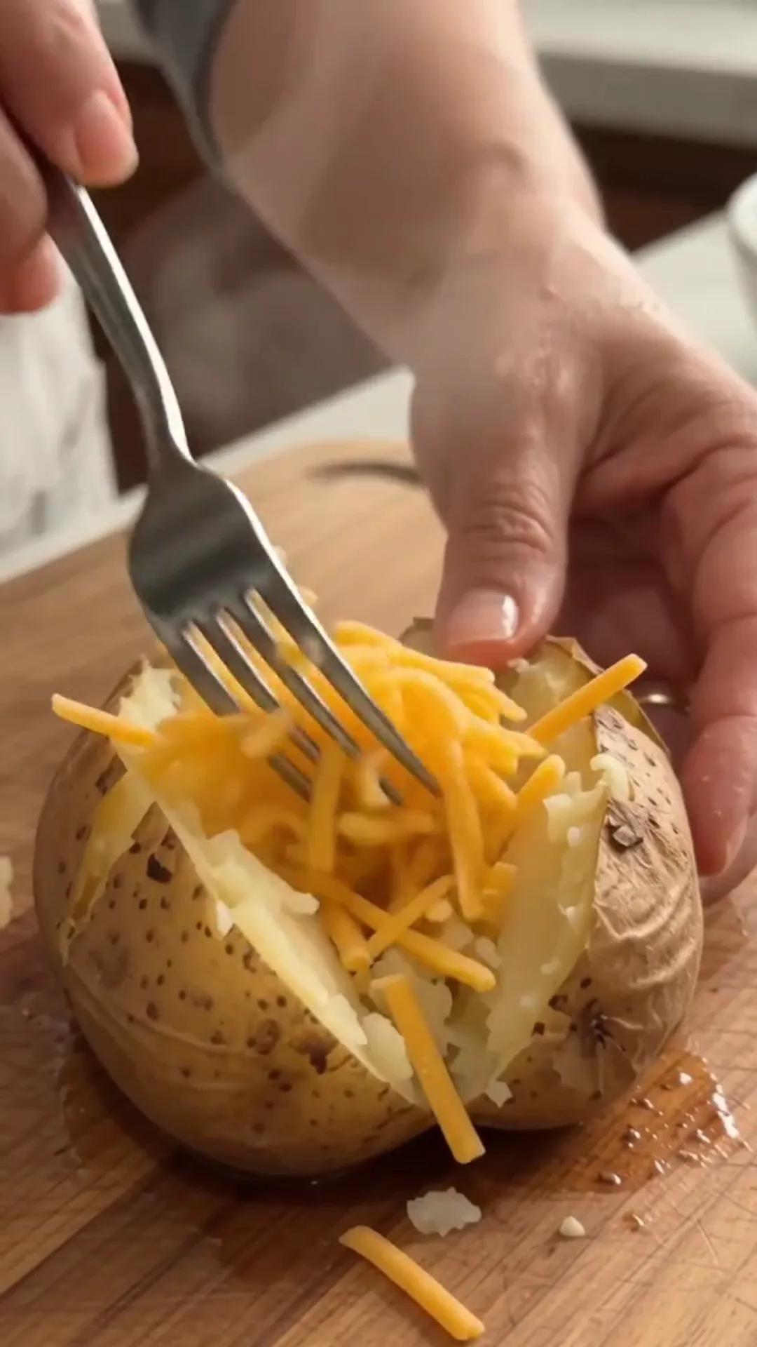 Garlic Butter Loaded Steak Baked Potatoes – Someone is adding cheese to a baked potato