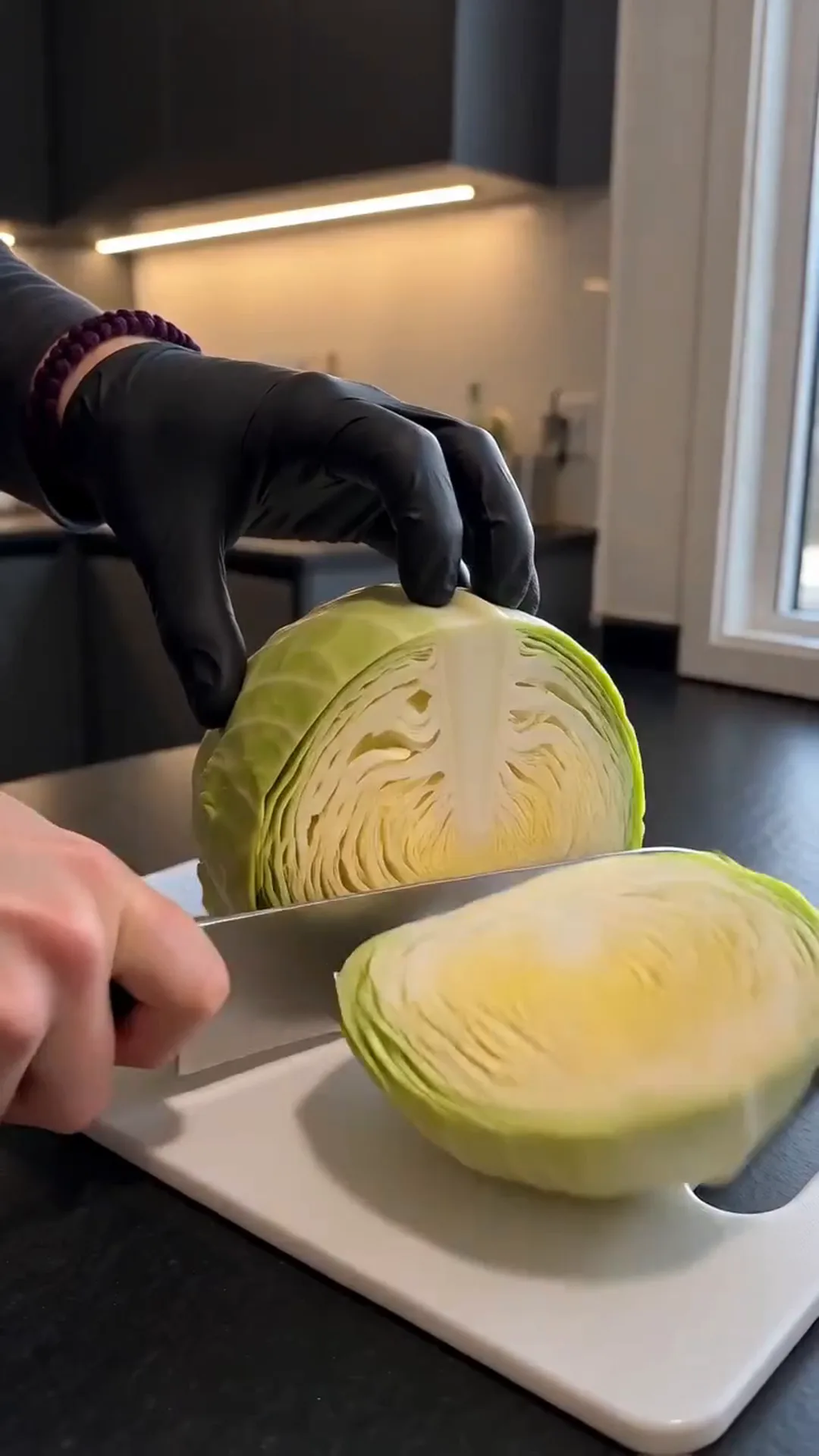 Golden Cheesy Baked Cabbage Steaks with Turkey Bacon – A person is cutting a cabbage on a white cutting board