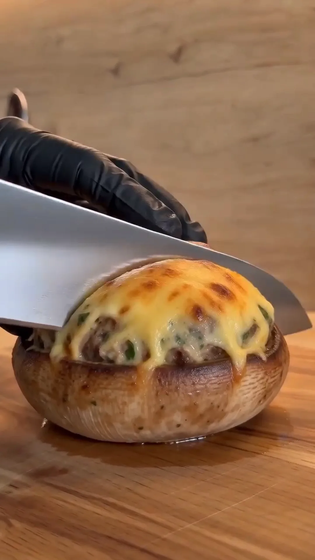 Golden Cheesy Chicken Stuffed Mushrooms Recipe – A hand is cutting a stuffed mushroom with a knife