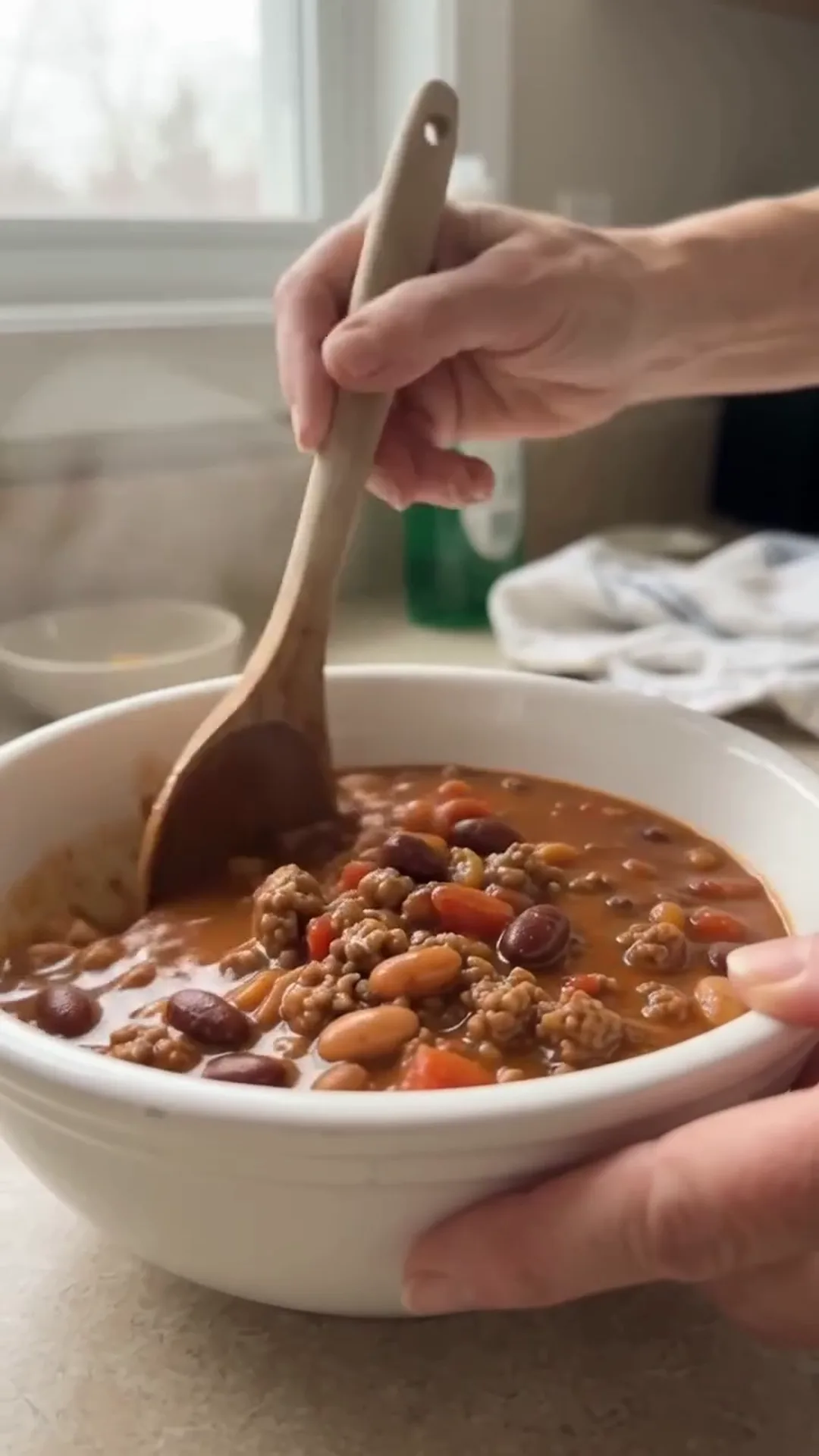 Hearty Slow Cooker Beef and Turkey Chili Recipe – Someone is stirring a bowl of chili with a wooden spoon