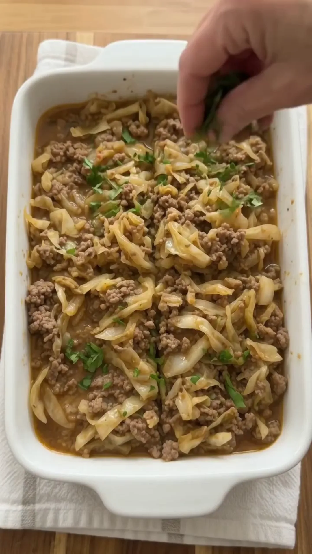 High Fiber Savory Cabbage and Ground Beef Skillet – hand placing food in a baking dish