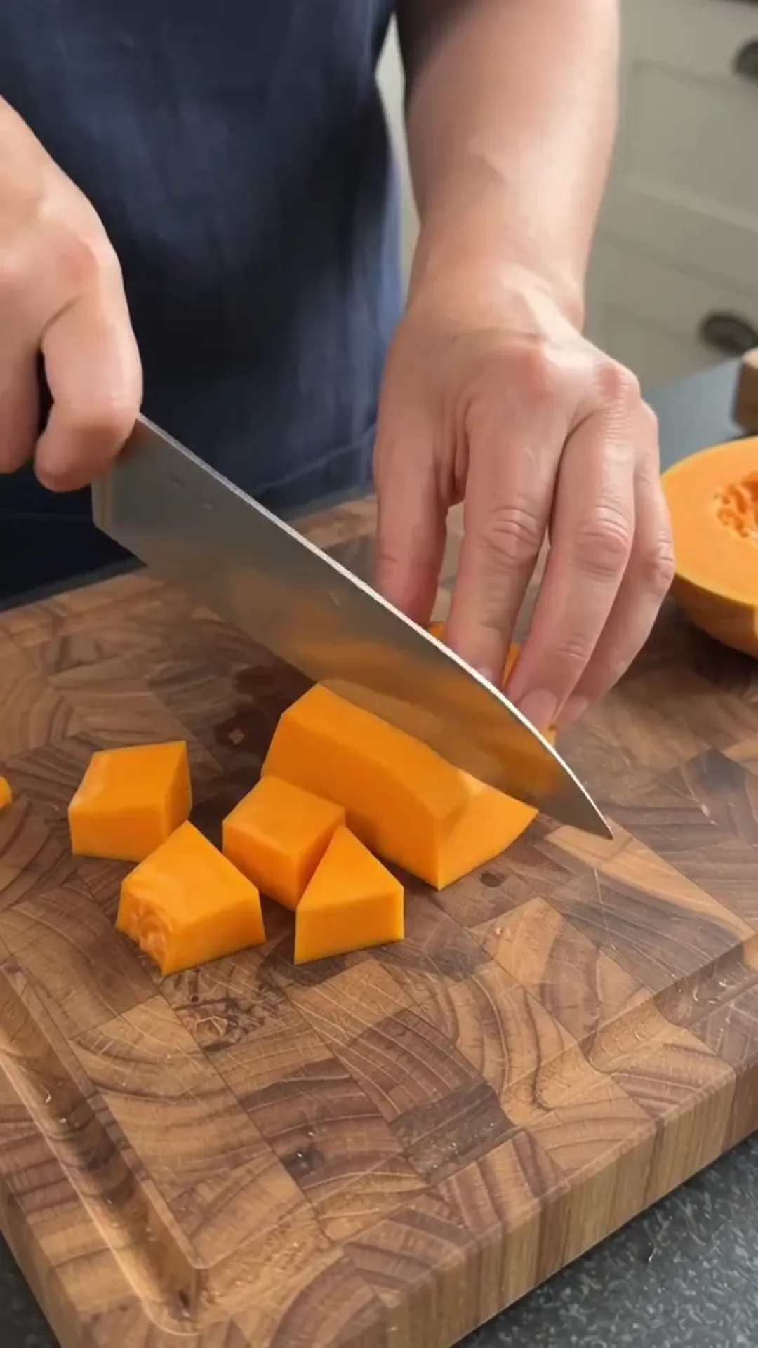 Honey-Glazed Salmon and Roasted Pumpkin Salad – A person is cutting a pumpkin on a wooden cutting board
