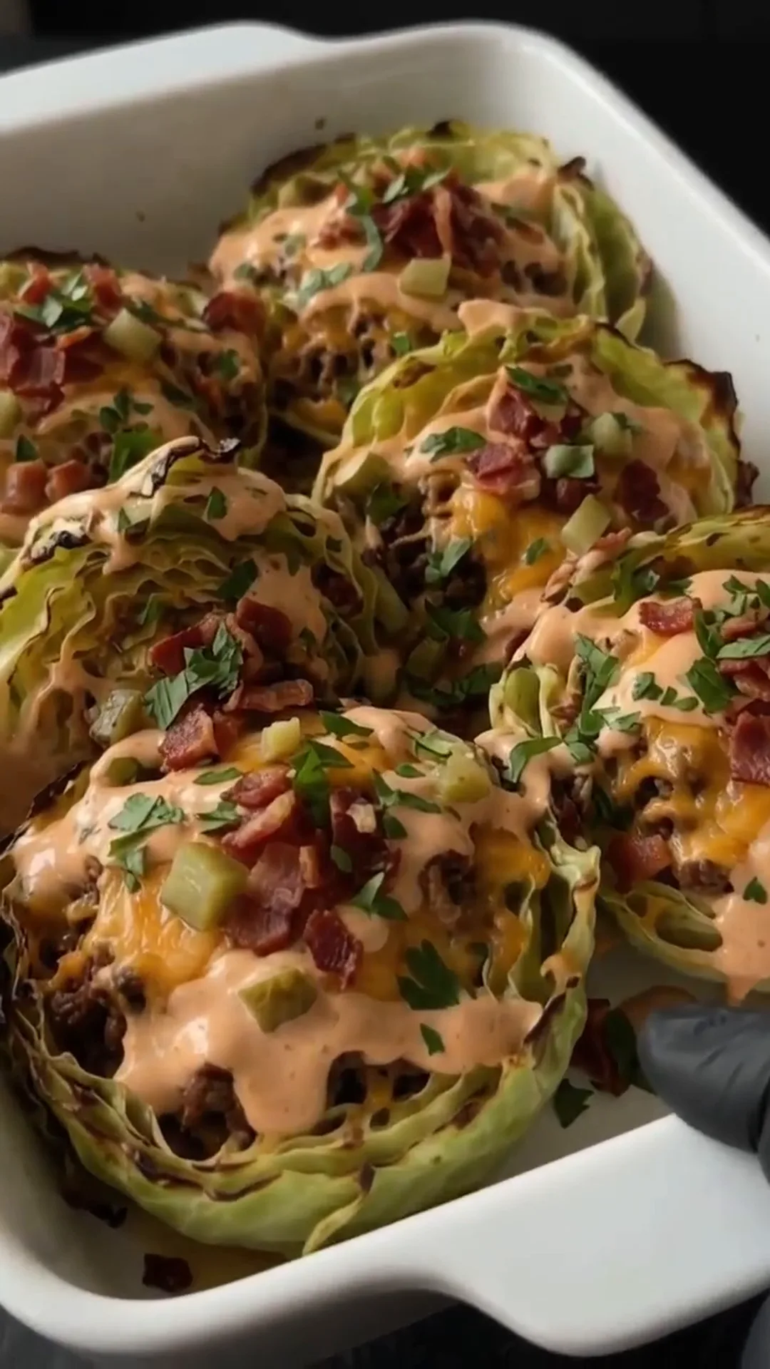 Savory Cheeseburger Cabbage Cups with Melted Cheese – Someone is holding a dish of cabbage topped with cheese and turkey bacon