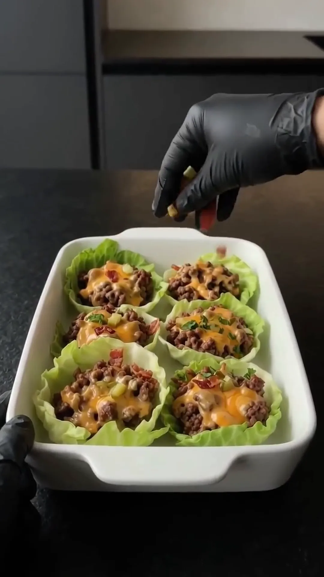 Savory Cheeseburger Cabbage Cups with Melted Cheese – A person is adding a topping to a dish