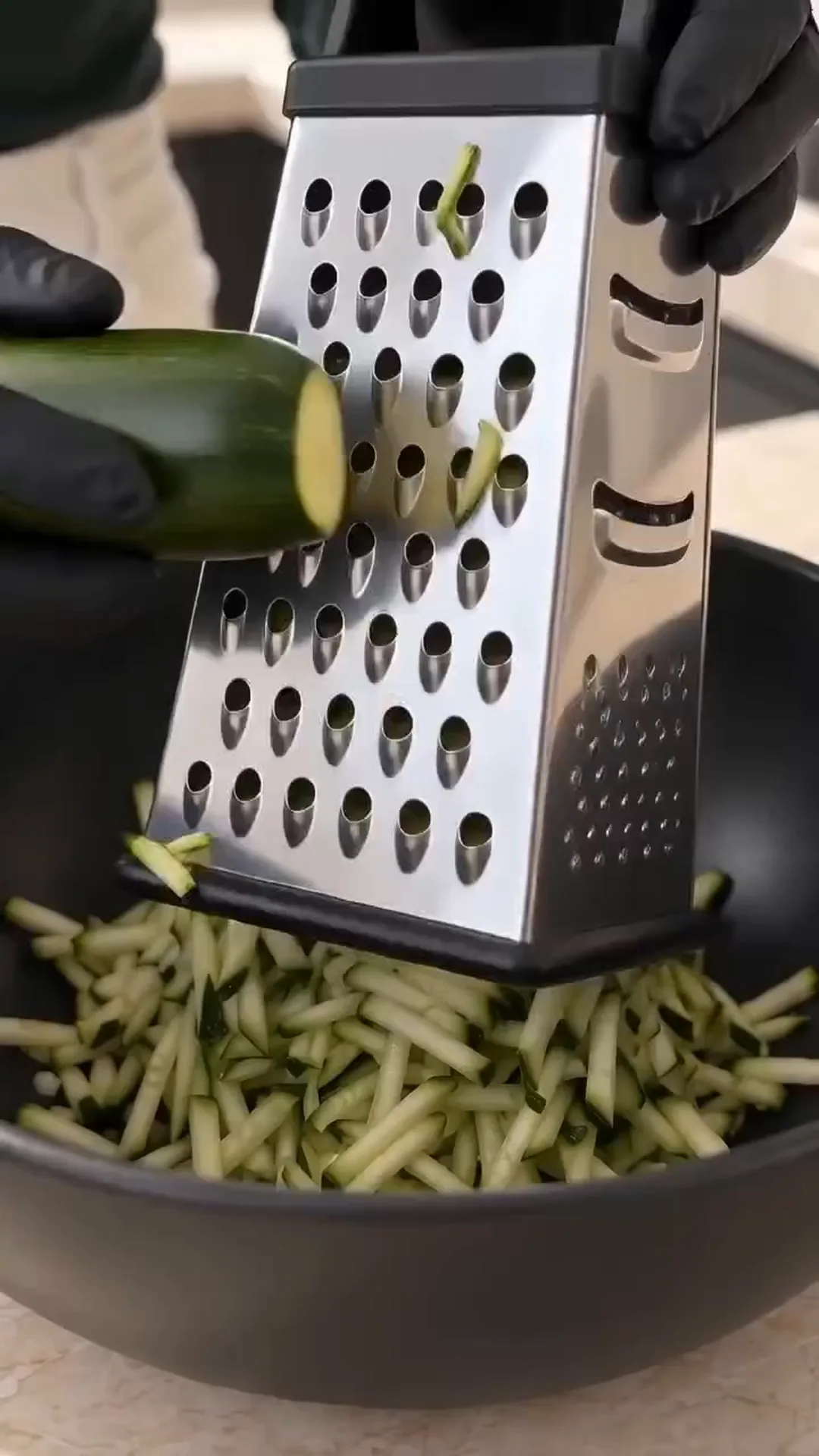 Savory Cheesy Baked Zucchini Loaf with Melted Center – A person is grating a zucchini into a bowl