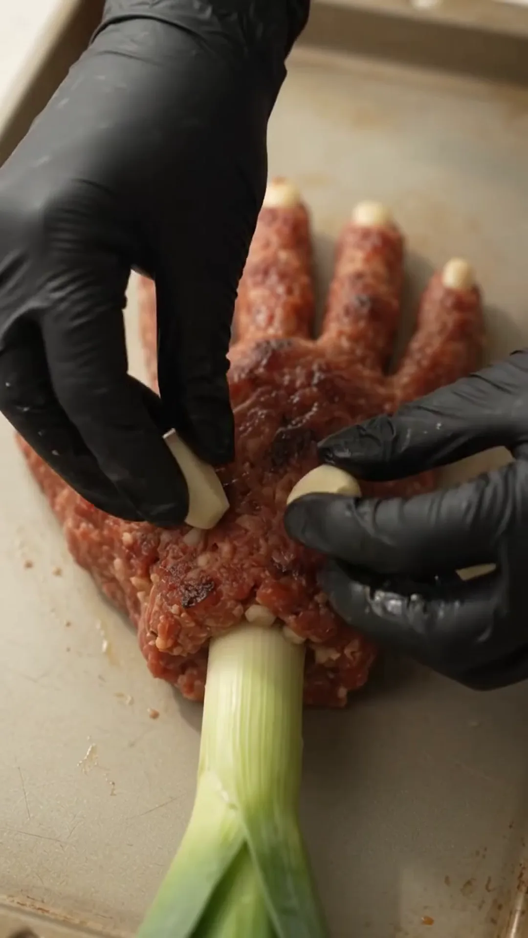 Spooky Halloween Hand Meatloaf Centerpiece – Hands are stuffing a green onion into raw meat
