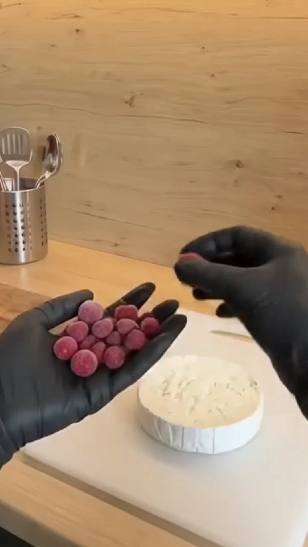 Warm Baked Camembert with Sweet Berries and Roasted Grapes – A person is preparing a cheese dish with frozen berries