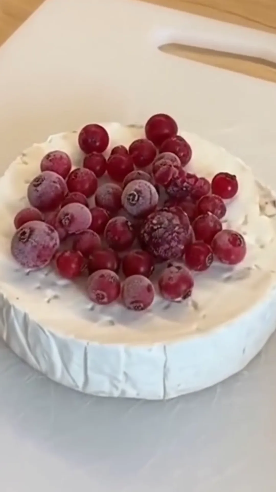 Warm Baked Camembert with Sweet Berries and Roasted Grapes – brie cheese topped with frozen cranberries, on a cutting board